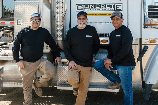values-trust Three construction professionals in branded attire stand confidently beside a truck, showcasing expertise in rebar and concrete supplies.